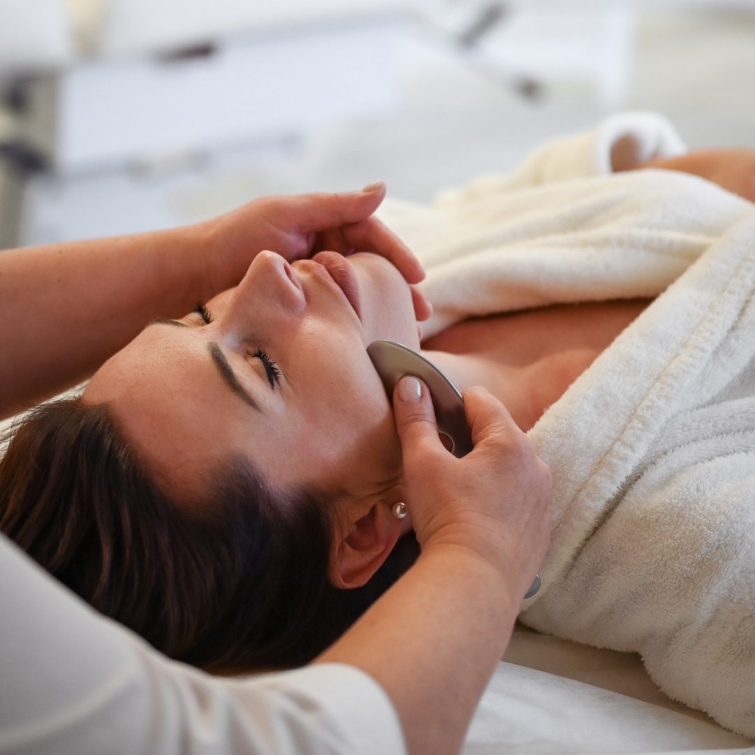 Woman receiving lymphatic drainage with a stainless steel gua sha to improve circulation, sculpt bones, and reduce inflammation.